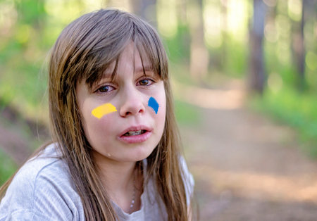 Sign of Ukrainian flag on child's cheek. Ukrainian geopolitics globe crisis. Close up kids face. Sadness longing hope. No war. Hope for the world. Anxiety and anticipation.の写真素材