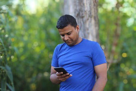 yong man standing with a tree using cellphone park outdoorの写真素材
