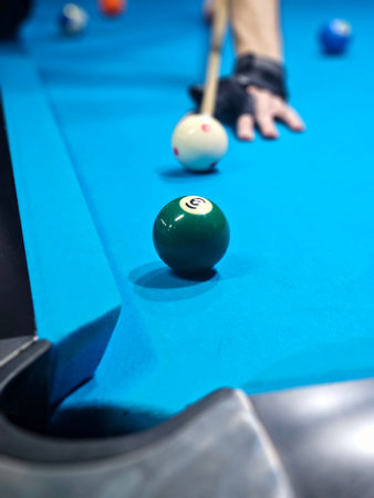 Billiard cue in hands of male player standing by pool table and concentrating before hitting white...