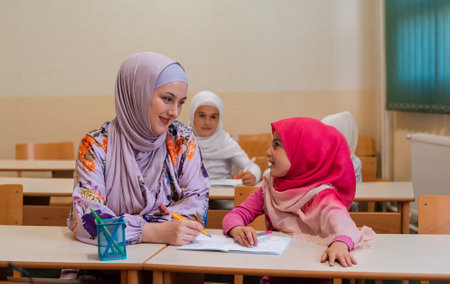 Female hijab Muslim teacher helps school children to finish the lesson in the classroom.の写真素材