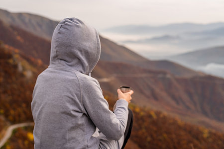 A happy traveler woman drinks a coffee or tea from a cup relaxing during a hike and enjoys the scenery in the mountains adventure travel.の写真素材