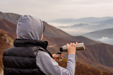 A happy traveler woman drinks a coffee or tea from a cup thermos bottle relaxing during a hike and enjoys the scenery in the mountains adventure travel.の写真素材