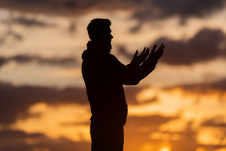 Silhouette of prayer having worship and praying with hands open at sunsetの写真素材