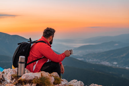 A man traveler enjoying while drinking a cup of coffee or tea on the mountain top during the hike, adventure travel.の写真素材