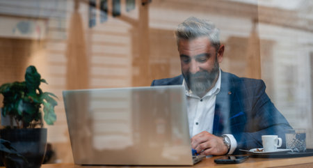 A happy mature business man sitting at his desk in the office or restaurant cafe near the window and...