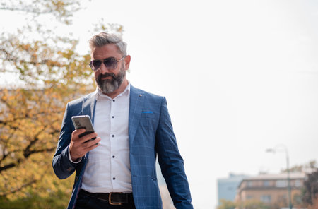 A handsome mature business man using mobile phone app texting in the city street.の写真素材