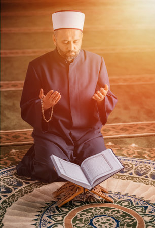 A Muslim prayer man praying with hands up while reading a Quran inside the mosque.の写真素材