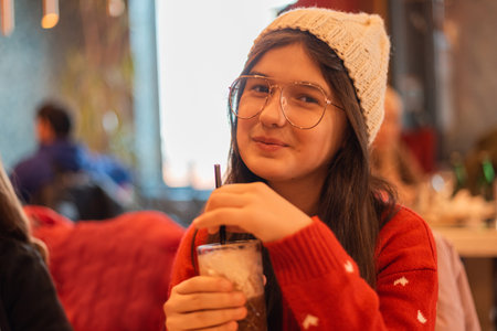A happy teenage girl enjoying while drinking a cup of coffee or cappuccino in the cafe restaurant looking at camera and smiling.の写真素材