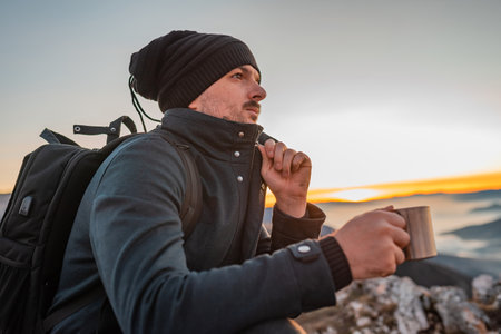 A male traveler drinking a cup of coffee during the hiking on the mountain.
