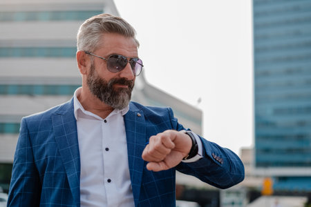 A busy mature business man looking at a wrist watch with an urban building in the background.の写真素材