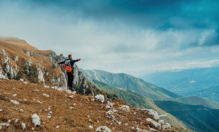A male climber with arms up celebrating successful completed route on the mountain top, adventure travel.の写真素材