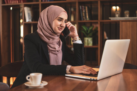 A happy Muslim business woman talking on her phone while working at the office.の写真素材