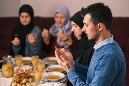 Muslim family making iftar dua to break fasting during Ramadan dining table at home together praying...
