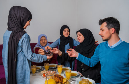 Happy Muslim family having iftar dinner at home during Ramadan dining table eating dates to break...