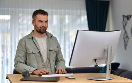 A happy man using a desktop computer while working at a home.
