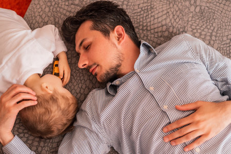 A young father shares love with his son and spends time together at home, lying and sleeping on the bed, top view.の写真素材