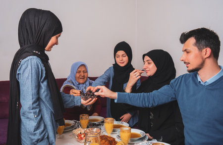 Happy Muslim family having iftar dinner at home during Ramadan dining table eating dates to break fast.の写真素材
