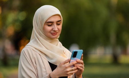 A young happy Muslim woman in hijab using a phone outsideの写真素材