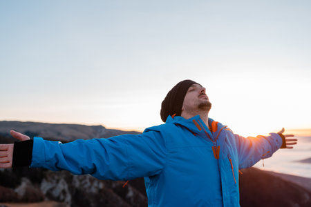 A carefree relaxing man deep breathing with arms outstretched and eyes closed in nature.