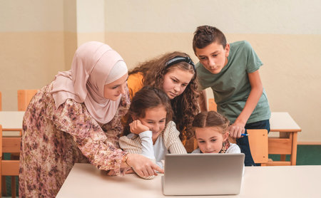 A female hijab teacher teaching group of child students using a laptop during the school class.の写真素材