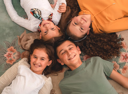 Happy group of children friends lying on the floor in a circle, looking at the camera, top view.の写真素材