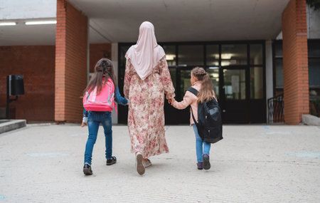 Hijab Muslim mother walking with holding hands her two child from school.の写真素材