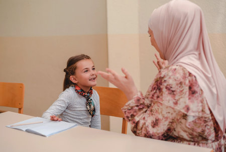 Female hijab teacher helps school kid to finish the lesson during the class in the classroom.の写真素材