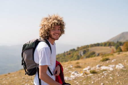 A young happy male traveler with curly hair enjoys while hiking or trekking trail mountain, active...