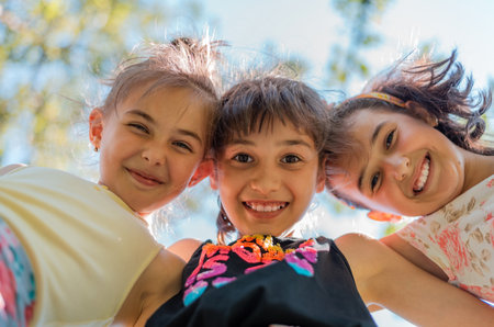 Directly below shot of happy children embracing each other having fun and smiling at camera with a sky background, a group of joyful kids playing together outside.の写真素材