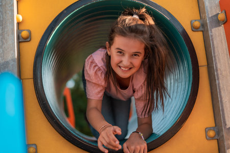 A happy kid girl playing on a slide on the park playground.の写真素材