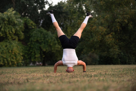 A fit man performing a headstand on grass in a park, showcasing strength, balance, and outdoor fitness activity.の写真素材