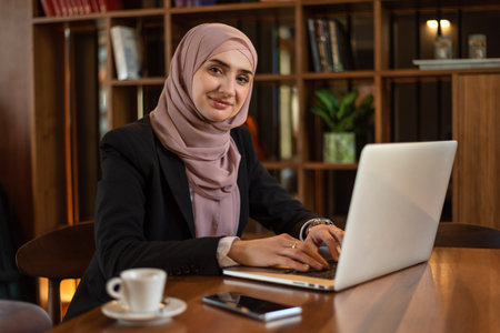 A happy Muslim business woman using a laptop while working at the office.