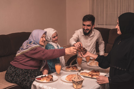 Happy Muslim family having iftar dinner during Ramadan dining table at home, sharing dates and...