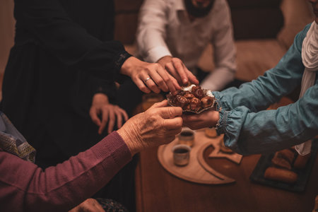 Hands Sharing Dates During Ramadan Celebration Close-Up View of Generational Muslim Family Members Enjoying Traditional Food Together During Iftar Meal at Homeの写真素材