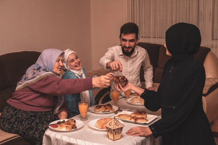 Happy Muslim family having iftar dinner during Ramadan dining table at home, sharing dates and smiling together.の写真素材