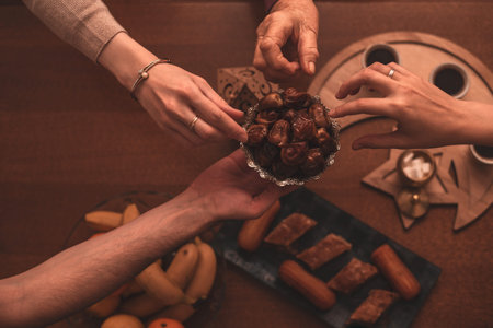 Hands Sharing Dates During Ramadan Celebration Close-Up Top View of Generational Family Members Enjoying Traditional Food Together During Iftar Meal at Home.の写真素材