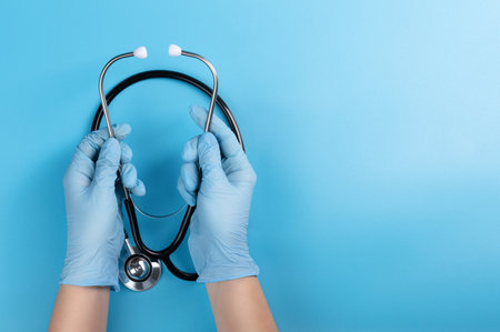 Doctor's hands in medical gloves hold a stethoscope on a blue background. Concept for the treatment and diagnosis of the respiratory and heart organs.の写真素材