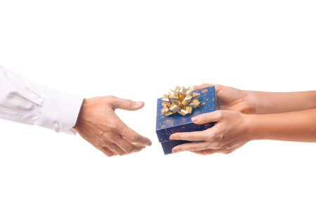 Hands of a girl give a gift in a blue box with a gold bow to a man in a white shirt, white isolated background. Concept of new year, Christmas or birthday partiesの写真素材