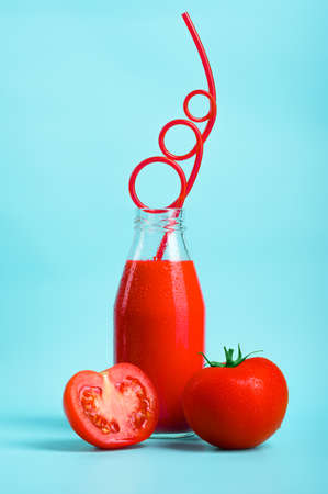 Cold tomato juice in a bottle with a beautiful straw and fresh tomatoes and slices on a blue background. The concept of an environmentally friendly and healthy drink from an organic farm.の写真素材
