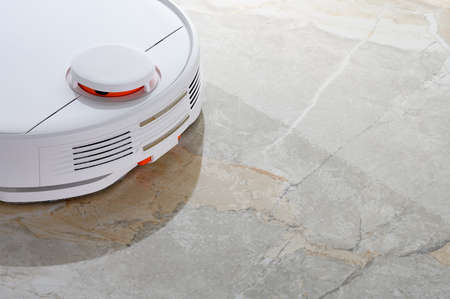 White robot vacuum cleaner with wet cleaning function, washes the floor of granite, very close-up.