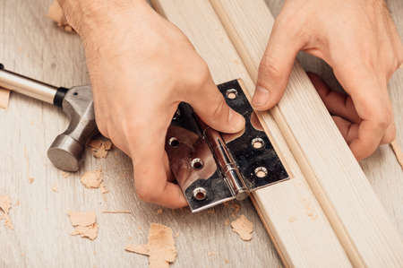 Hands of the master installing the door hinge with a hand tool, close-up warm tones top view.の写真素材