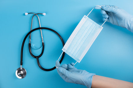 Doctor's hands in medical gloves with a medical mask on the background of a stethoscope lying on the table.の写真素材