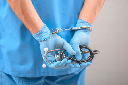 A medical officer, doctor, or quack in a blue medical uniform in handcuffs. The concept of crimes...
