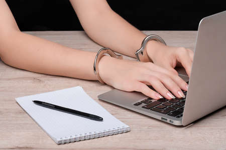 Hands cuffed on the keyboard of a laptop against the background of a Notepad with a pen. The concept of restricting journalistic activity or freedom of speech.の写真素材
