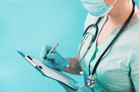 A masked doctor with a stethoscope and tablet fills out a medical history or prescribes a...