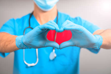 A medical officer or doctor in a medical blue uniform and gloves shows a heart sign colored redの写真素材