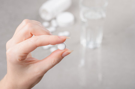 The girl holds a white tablet or vitamins or food Supplement in her hand, against the background of a table with a bubble and a glass of water. Concept of treatment, prevention of diseases or diet.の写真素材