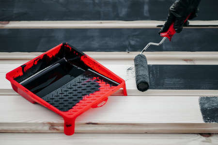 A man or woman wearing protective gloves, using a red roller and a paint bath, paints the Board black, the side view is very close.の写真素材