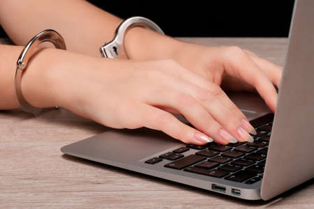 A girl in handcuffs is working on a laptop. The concept of censorship or restriction of freedom of speech. Very close-up.の写真素材
