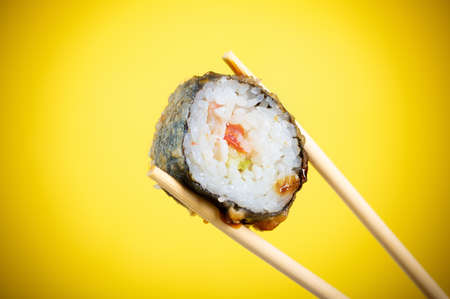 Sushi rolls close-up in wooden sticks on a bright yellow gradient backgroundの写真素材